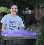 Vaughn Vaios Arambatzis smiling and standing behind a purple lidded recycle bottle wheelie bin