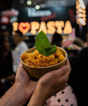 Two hands casping a bowl of pasta with a I love pasta sign in the background
