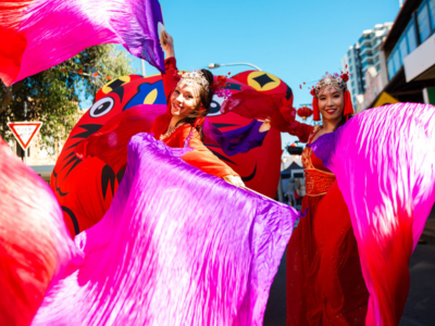 Girls in bright cultural costumes dancing with bright pink, red and purple flags.