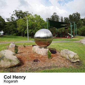 A spherical silver sculpture sits in a park in front of a playground.