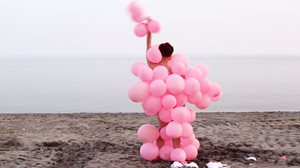 model on the beach wearing a pink costume made out of balloons