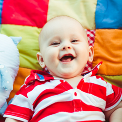 Baby smiling on colourful quilt.