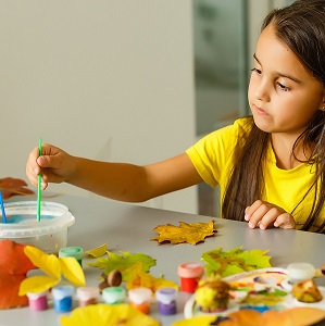 Girl with brown hair and yellow top is painting leaves.