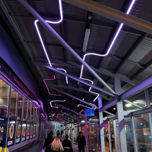 Interwoven purple light installation on celling with people walking beneath it