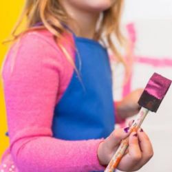 A girl holding a sponge brush with pink paint on it.