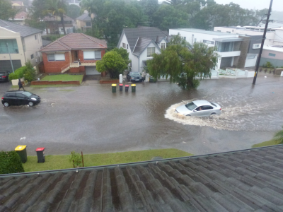 Deep flooding on a suburban street and a white car driving through the flooded water