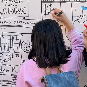 A girl with her back to the camera colouring in a black and white mural.