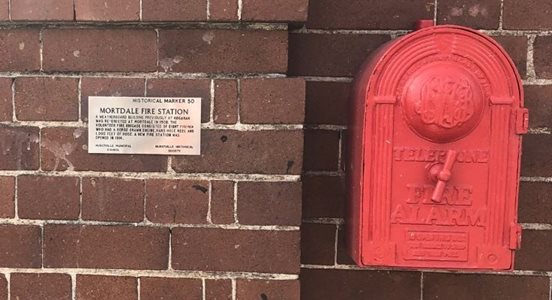 Mortdale Fire Station silver marker attached to brick wall next to red fire alarm