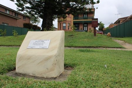 Site of Ithiel silver marker in small sandstone block with green lawn and a house in the background
