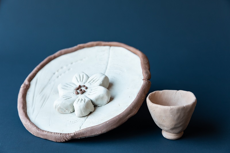 Two clay art pieces featuring a cup and a plate with a flower.