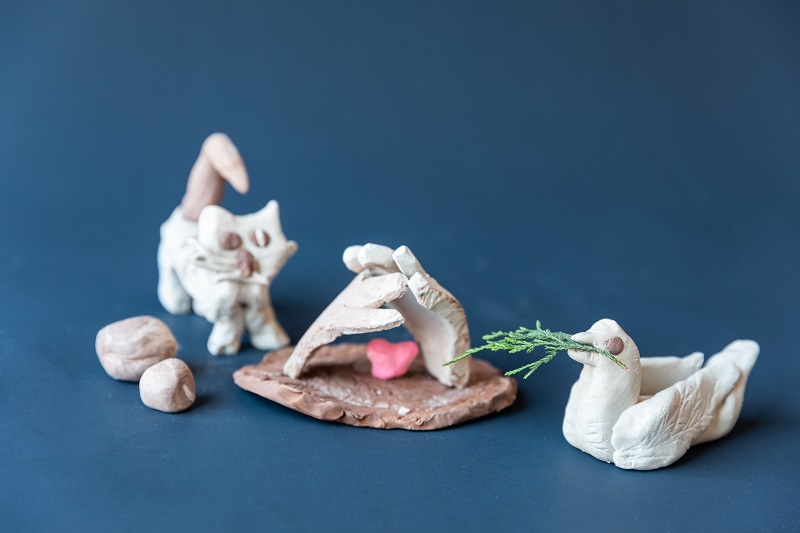 Clay artwork featuring a cat, dove and two hands.
