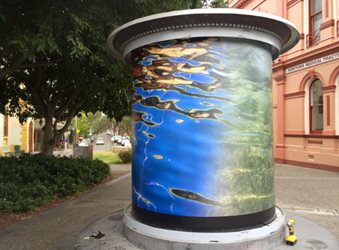 A large cylinder decorated with an blue, green, yellow and brown swirling artwork