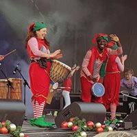 Two musicians dressed up as Christmas elves playing drums and smiling