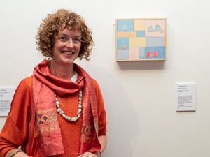 Artist Annabel Butler standing next to her artwork hung on a white gallery wall