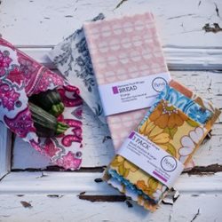 Different coloured beeswax wrap packs, with one shown wrapping a bunch of zuchinis.