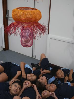 school children lying in the floor to see a different perspective of a weaved artwork