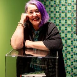The artist, Dr Nicola Hooper, smiling at the camera. Bright green wallpaper in background.