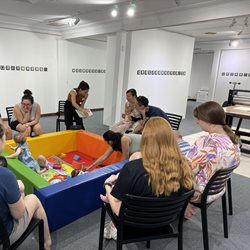 A group of people surrounding a foam sensory pit with babies in it at an art gallery.