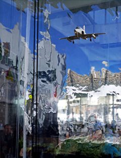 A distorted photograph showing reflections of shop fronts and an aeroplane in a glass window
