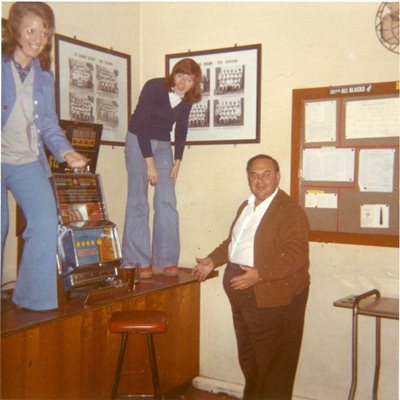 two ladies on top of a table and a surprised man look at the camera, they are part of the Rugby club that owned the building in the seventies