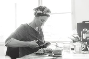 white and black photo of artist Sophie Lieu working on her studio while cutting up some materials