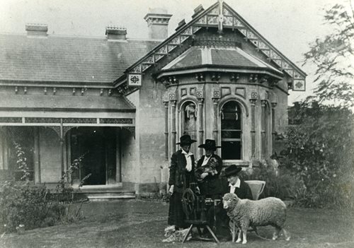 black and white picture of two ladies and a sheet in front of a victorian house, picture from 1890-1899