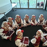 Young girls sitting in a circle smiling at the camera wearing traditional Macedonian clothes