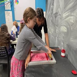 A girl and a teacher doing a pink linocut print.