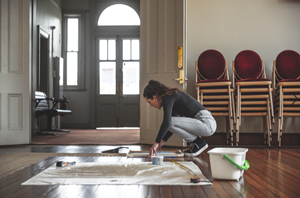 artist setting up her artwork of sand inside a room with wood floor